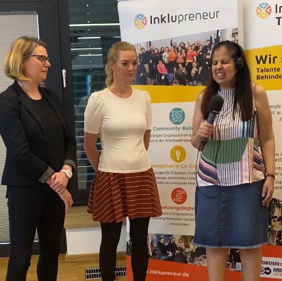 Zwei Mitarbeitende von Fraunhofer Mevis, Cynthia Budnick und Isabel Köster stehen im Halbkreis in einer Interviewsituation mit Amy Zayed von Inklupreneur. Hinter Ihnen stehen zwei Inklupreneur Talent-Pool Aufsteller. Die Aufmerksamkeit liegt bei Amy.