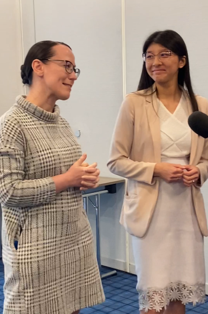 Zwei Mitarbeitende von Radisson Blu Angelika Saul links und Adelina Nguyen Van rechts, stehen vor einem neutral hellen Hintergrund. Am rechten Bildschirmrand ist der Kopf eines Mikrophons zu sehen.